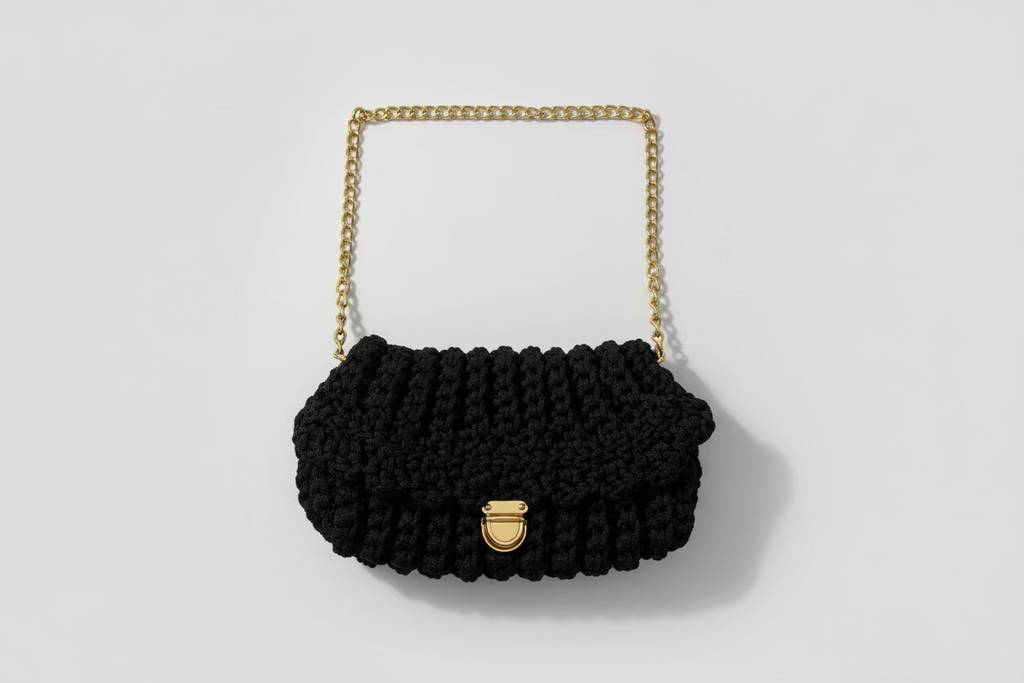 Black knitted handbag with a gold chain strap on a floral-patterned fabric background