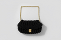 Black knitted handbag with a gold chain strap on a floral-patterned fabric background