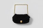 Black knitted handbag with a gold chain strap on a floral-patterned fabric background