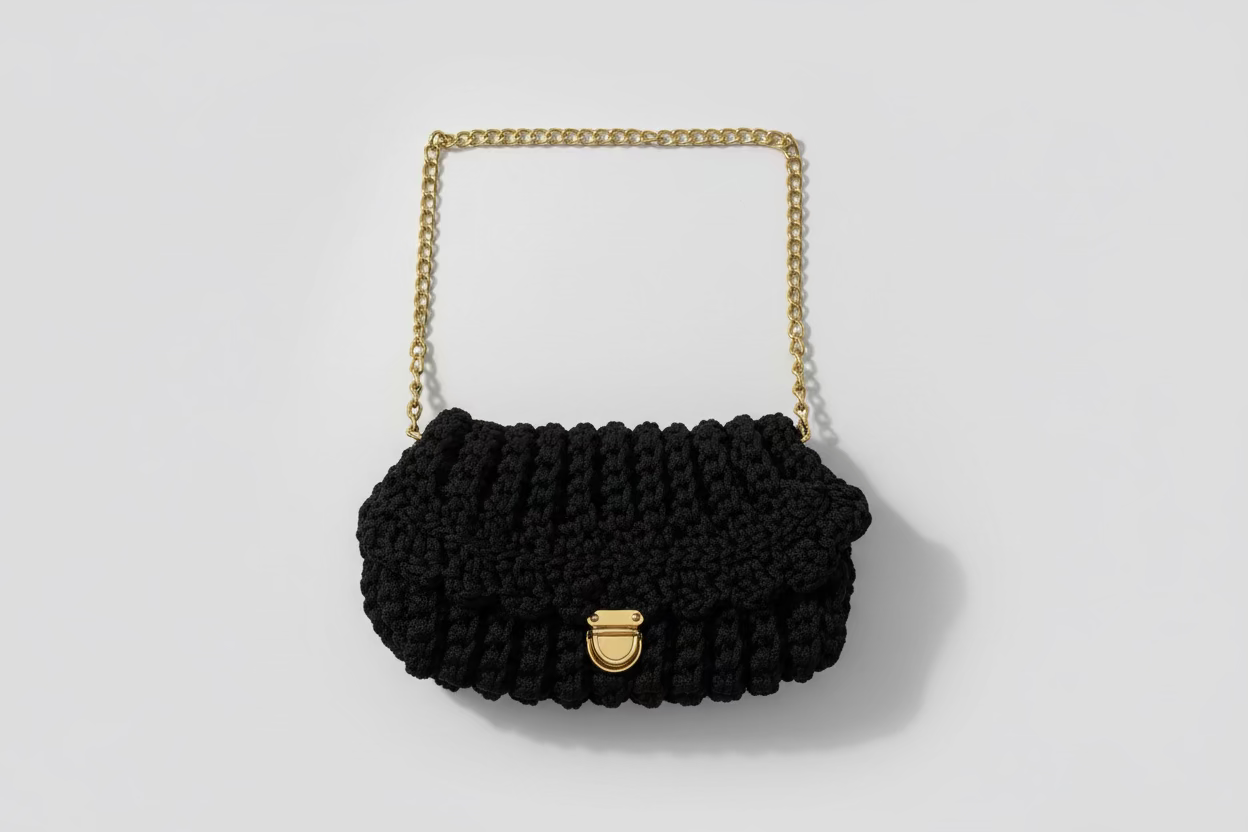Black knitted handbag with a gold chain strap on a floral-patterned fabric background