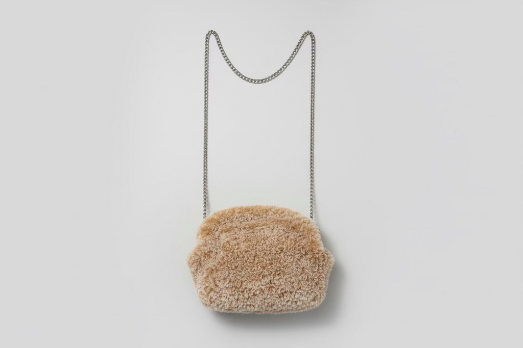 Brown fur handbag with a chain strap on a floral-patterned fabric background